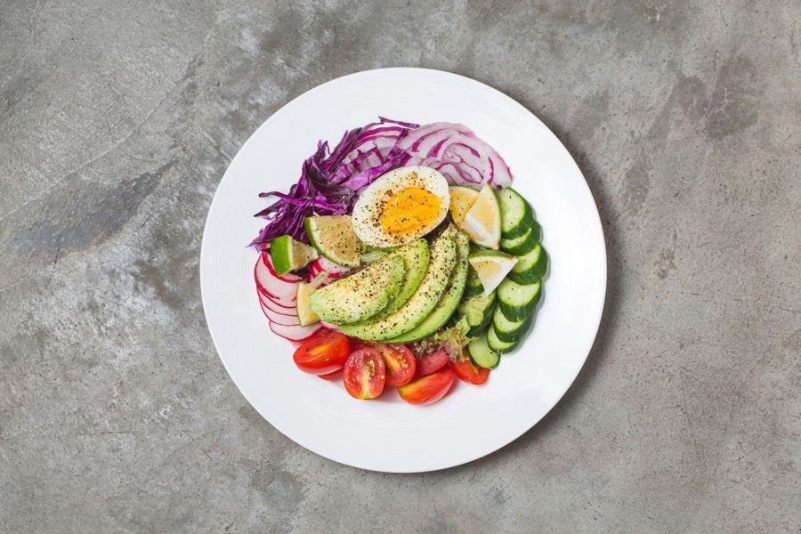 Plato saludable con aguacate, huevo, pepino, tomate y repollo morado